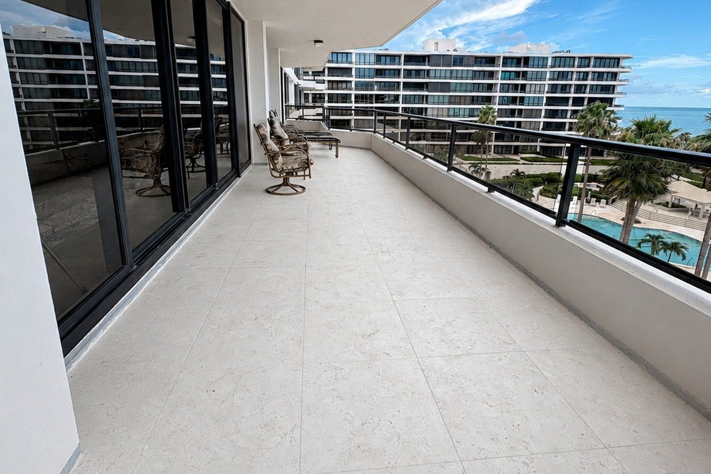 High-rise balcony with a light stone floor, looking over a pool to the water